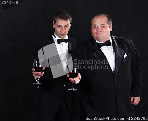 Image of Two stylish businessman in tuxedos with glasses of red wine