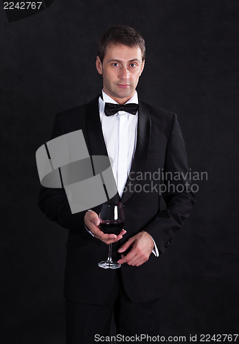 Image of Stylish man in elegant black tuxedo with glass red wine