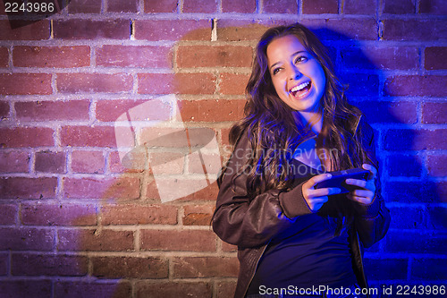 Image of Mixed Race Woman Using Her Cell Phone Against Brick Wall