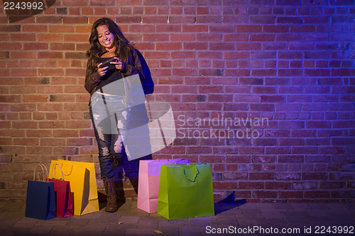 Image of Woman with Shopping Bags Using Cell Phone Against Brick Wall