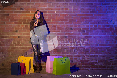 Image of Woman with Shopping Bags Using Cell Phone Against Brick Wall