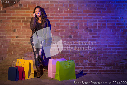 Image of Woman with Shopping Bags Using Cell Phone Against Brick Wall