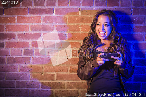 Image of Mixed Race Woman Using Her Cell Phone Against Brick Wall