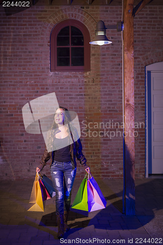 Image of Mixed Race Young Woman Walking Carrying Shopping Bags at Night