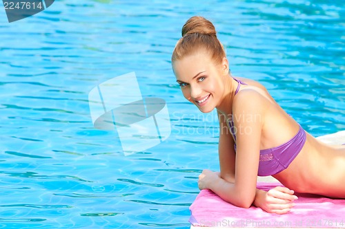 Image of Young woman in swimsuit lying close to pool