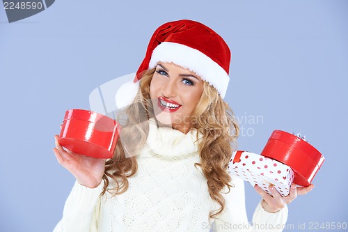 Image of Smiling woman in Santa hat holding Christmas gifts