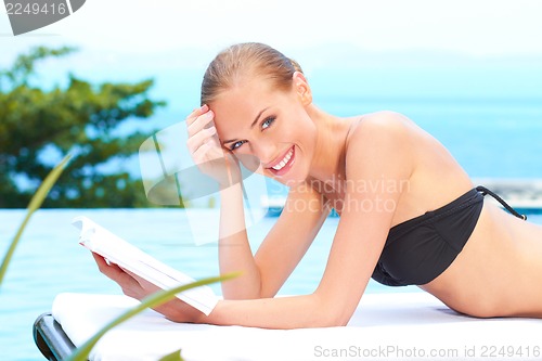 Image of Woman reading a book next to swimming pool