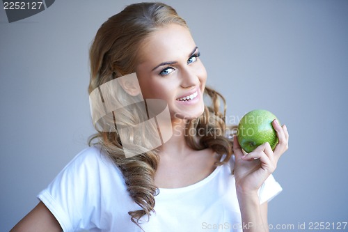 Image of Head shot of woman holding green apple against grey