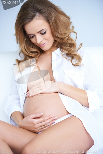 Image of Beautiful pregnant woman sitting on couch