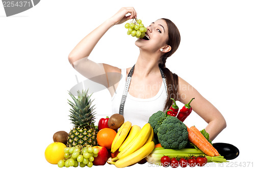 Image of Young smiling girl eating grapes, looking at camera