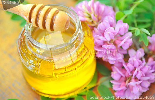 Image of glass jar full of honey and stick with acacia pink and white flo