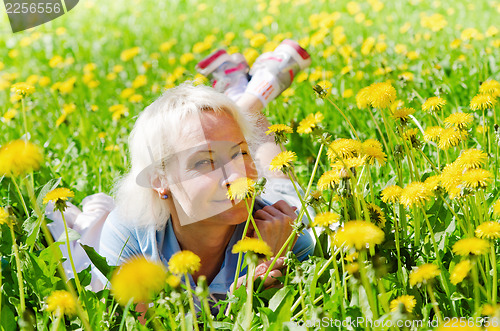 Image of A woman lies in a clearing and sniffs a flower  