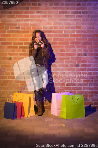 Image of Woman with Shopping Bags Using Cell Phone Against Brick Wall