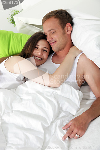 Image of Smiling woman cuddling her husband in bed