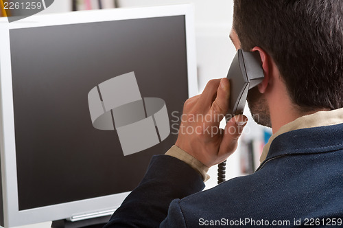 Image of Casual Businessman Talking over the Phone and Looking at a Compu