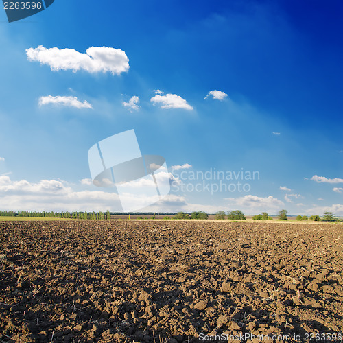 Image of black ploughed field under deep blue sky with clouds