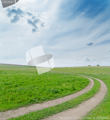 Image of green field with dirty road under cloudy sky