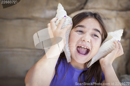 Image of Young Girl Playing with Large Sea Shells Against Her Ears