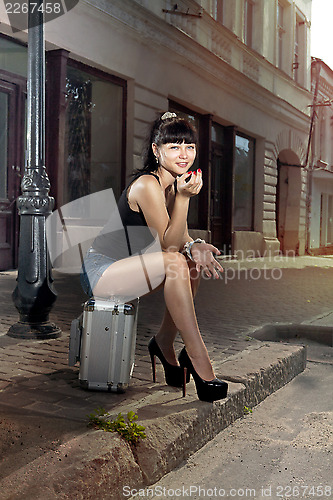 Image of woman sits on suitcase near road