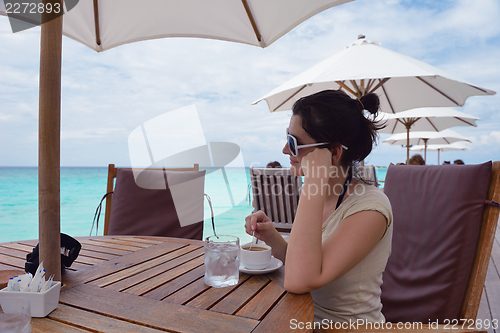 Image of Beautiful young woman with a drink by the sea