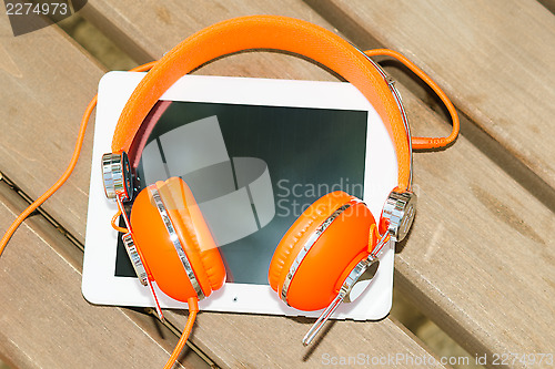 Image of White tablet PC with orange headphones on the wood bench