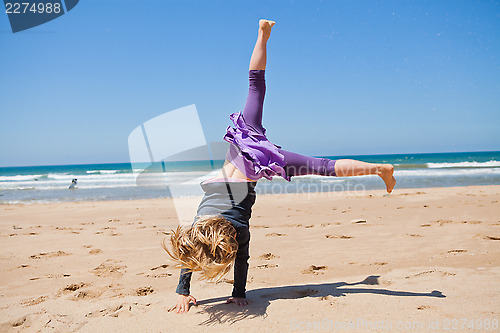 Image of Young girl doing cartwheel at beach