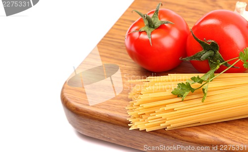 Image of uncooked spaghetti, garlic and tomatos on a preparation board are located left