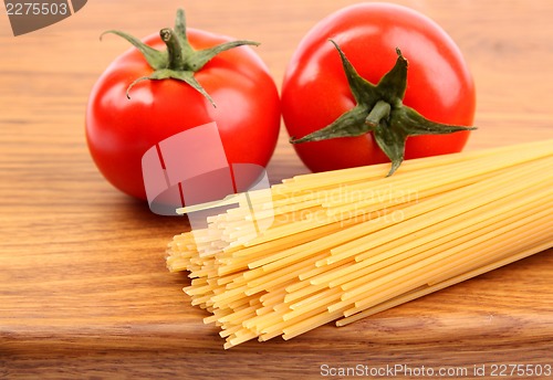 Image of Tomatoesl and uncooked spaghetti on a cutting board