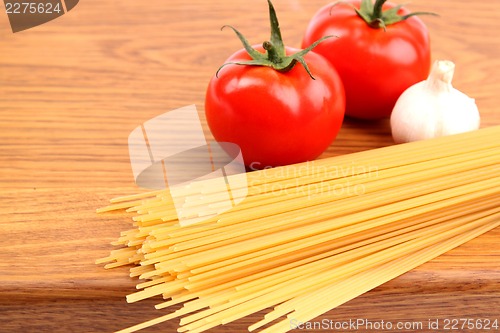 Image of uncooked spaghetti, garlic and tomatos on a preparation board