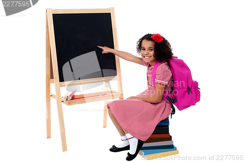 Image of Cute smiling student pointing at blank chalkboard