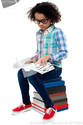 Image of Young kid sitting on stack of books and reading