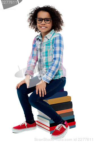 Image of School girl sitting on stack of books