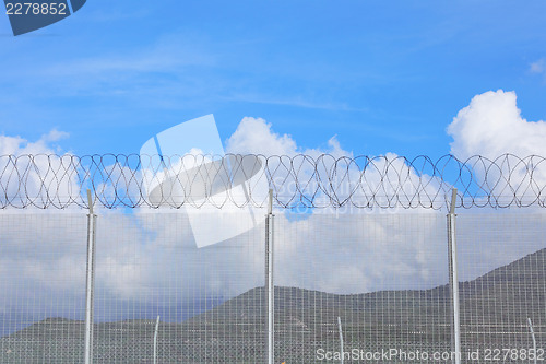 Image of Chain link fence with barbed wire under blue sky