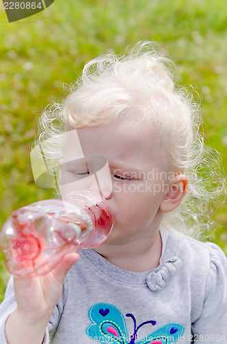 Image of The small blond girl drinks water from a bottle, a close up