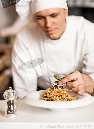 Image of Chef decorating pasta salad with herbal leaves