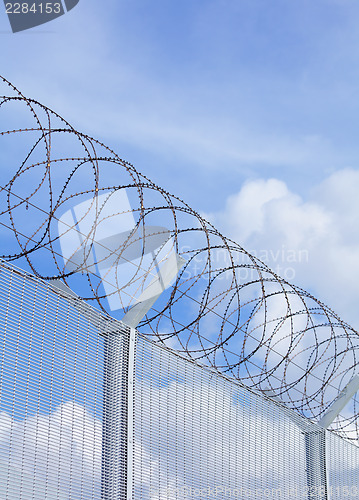 Image of Chain link fence with barbed wire under blue sky