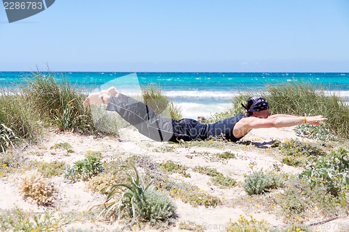 Image of man doing pilates exercises on beach in summer