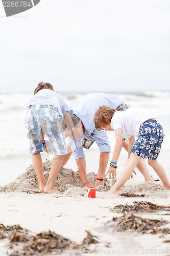 Image of father and sons on the beach playing in the sand
