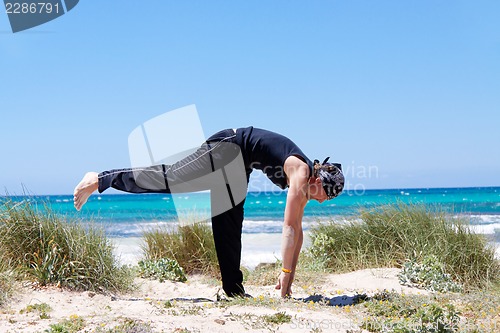 Image of man doing pilates exercises on beach in summer