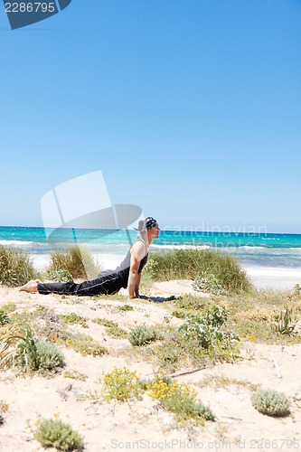 Image of man doing pilates exercises on beach in summer