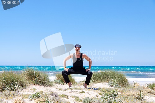 Image of man doing pilates exercises on beach in summer