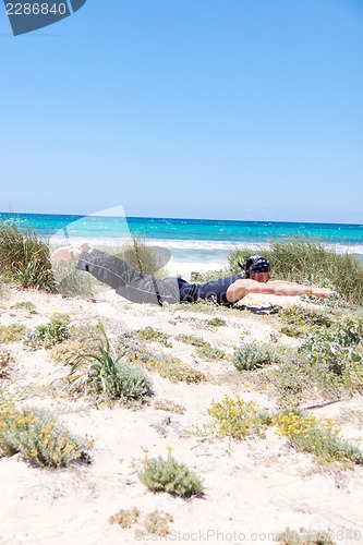 Image of man doing pilates exercises on beach in summer