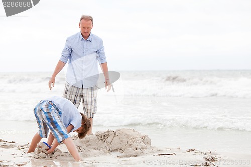 Image of father and sons on the beach playing in the sand
