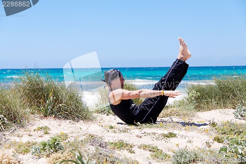 Image of man doing pilates exercises on beach in summer