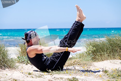 Image of man doing pilates exercises on beach in summer