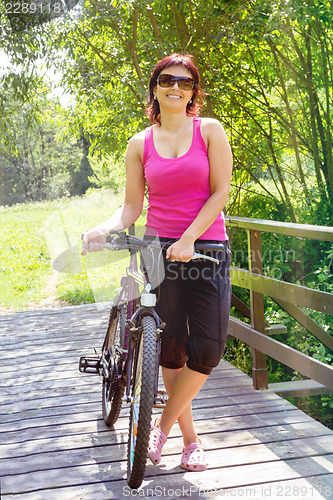 Image of pretty woman with bicycle on small wooden bridge