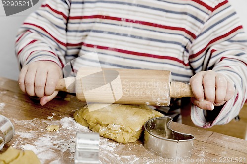 Image of child rolling dough on wooden desk