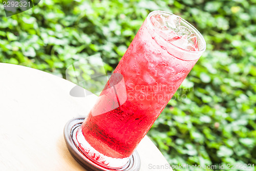 Image of Glass of iced sweet red drink on green background