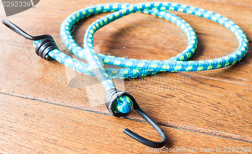 Image of Blue elastic rope with metal hooks on wood background