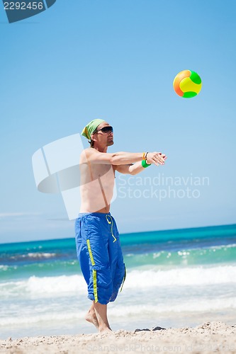 Image of attractive young man playing volleyball on the beach